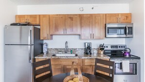 A compact kitchen with wooden cabinets, a stainless steel refrigerator, a microwave, a stove, and a sink. - Ocean View Waikiki Condo with Free Parking -- Short Walk to Beach (Honolulu)