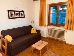 Ein Wohnzimmer mit einer Couch, einem Holztisch, einem Heizkörper und einem Fenster mit Vorhängen.