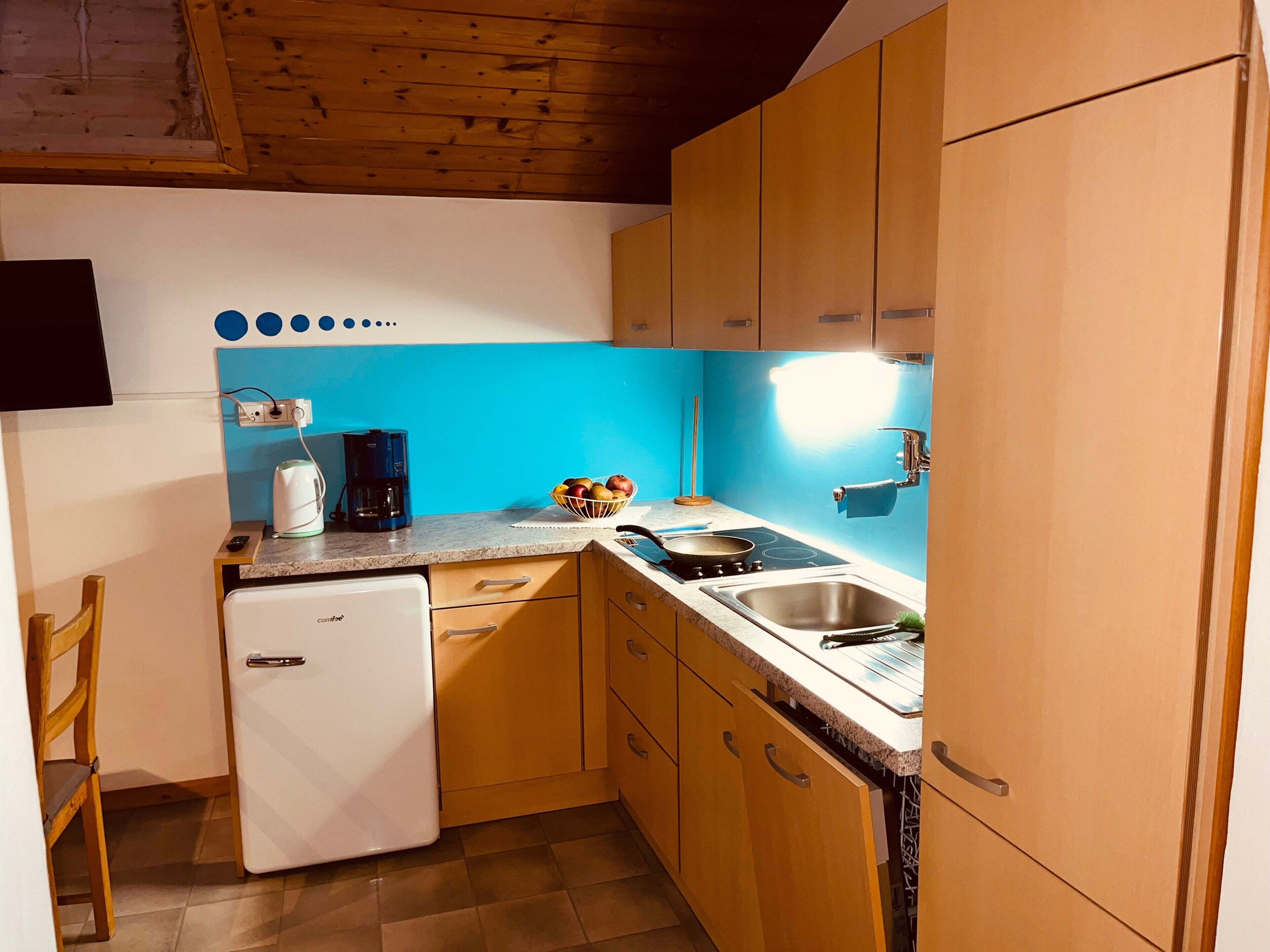 A compact kitchen with a refrigerator, coffee maker, sink, and a blue backsplash.