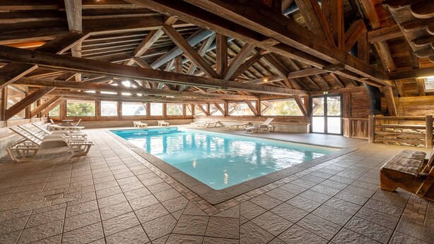 An indoor swimming pool with wooden beams, tiled floor, and lounge chairs. - Apartment 'Lapon H10' with Mountain View and Balcony (Hauteluce)