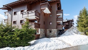 A multi-story wooden building with balconies, stone lower levels, and snow accumulation. - Apartment 'Lapon H10' with Mountain View and Balcony (Hauteluce)