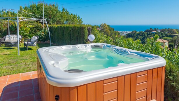 Een hottub met een houten buitenkant, omringd door een terras met tuinmeubilair.