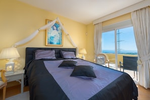 A bedroom with a bed, a nightstand, a chair, a window with curtains, and a balcony with a chair. - Penthouse Studio Apartment 'Roca Penthouse' with Sea View, Wi-Fi and Air Conditioning (Estepona)