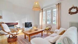 A cozy living room with a wooden coffee table, wicker chairs, a sofa, and a television. - Fleur D'ajonc - Locoal Mendon (LOCOAL MENDON)