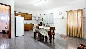Une cuisine avec des meubles de rangement en bois, un réfrigérateur blanc, une table à manger avec des chaises et une horloge au mur.