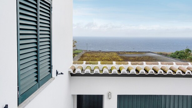 Un balcon avec vue sur l’océan, une façade blanche et un toit recouvert de tuiles.