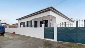 Une maison blanche avec un toit en tuiles, une entrée fermée par un portail et une voiture garée.
