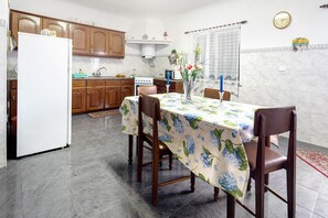 A kitchen with wooden cabinets, a white refrigerator, a dining table with a floral tablecloth, and a vase with flowers.