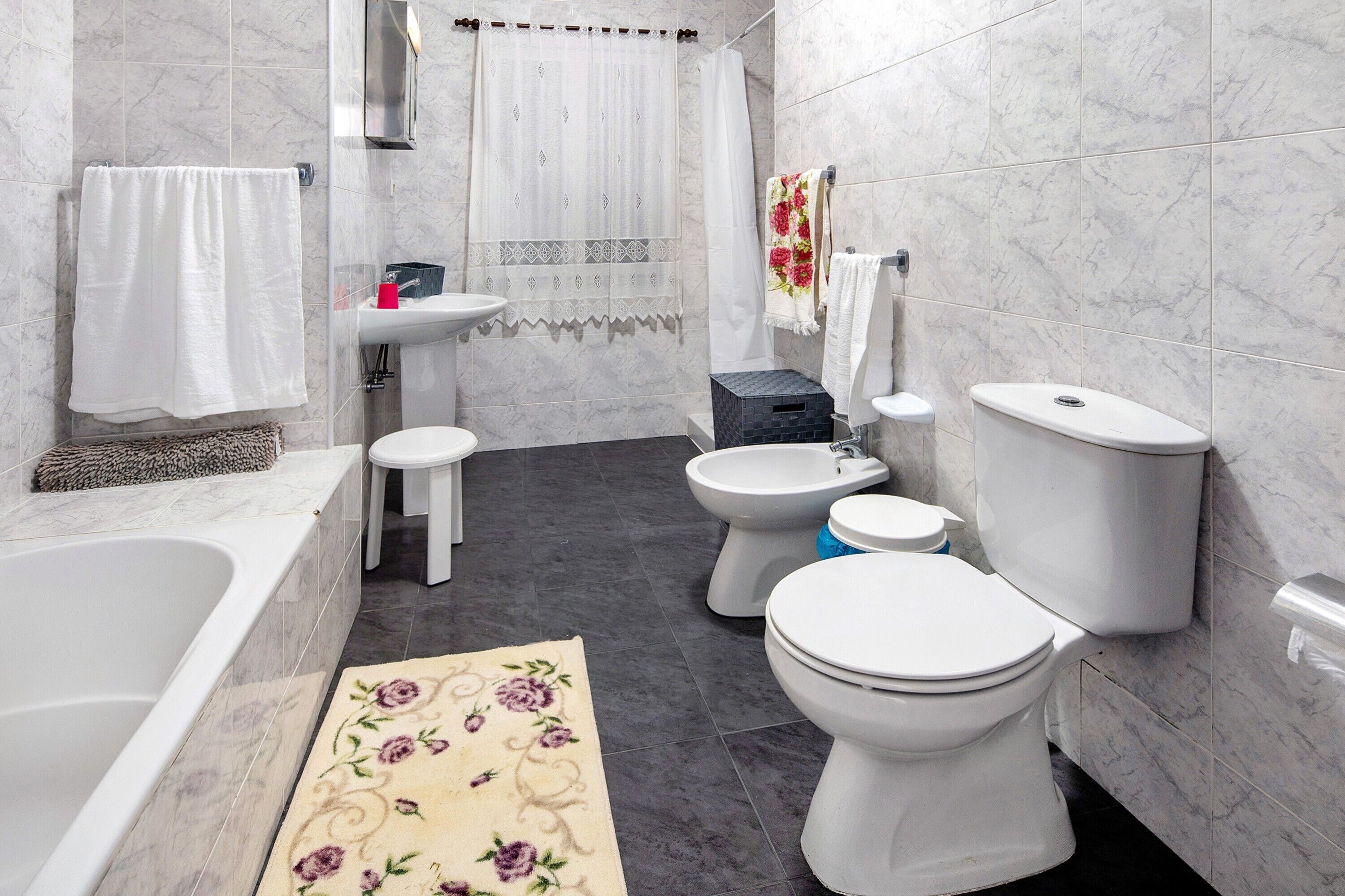 A bathroom with a bathtub, two toilets, a bidet, a sink, and a shower curtain.