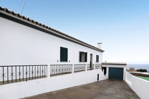 A white building with a tiled roof, a black metal railing, and a green door.