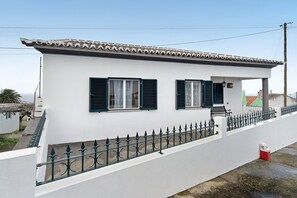 A white building with green shutters, a balcony, and a metal fence.