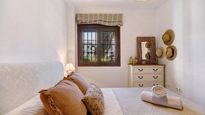 A bedroom with a bed, pillows, a bedside table, a mirror, and a window with a view.