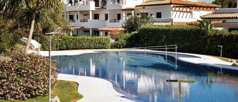 Una piscina con borde curvo, rodeada por un césped cuidado y un edificio grande con varios balcones.