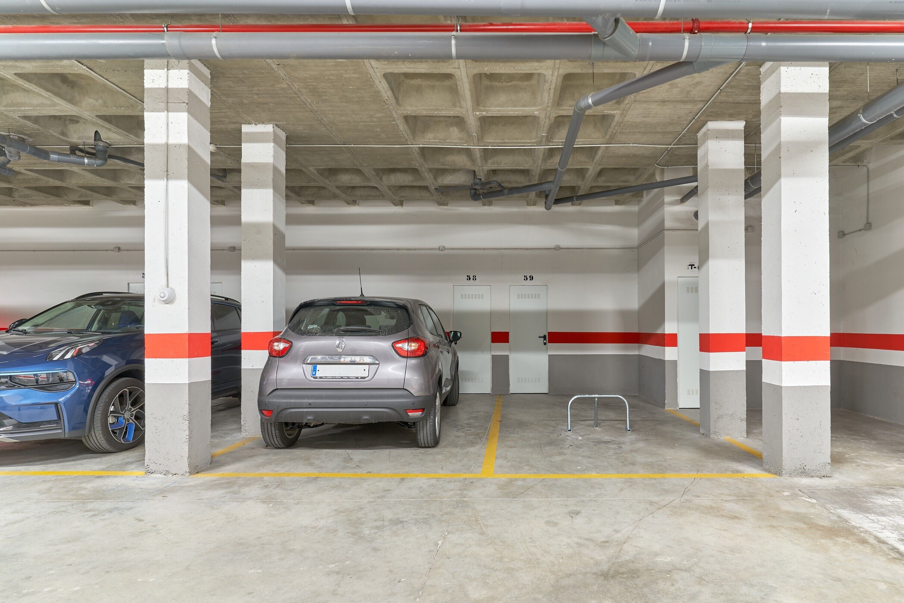 Eine Tiefgarage mit Betonpfeilern, zwei geparkte Autos und einer Wand mit roten und weißen Streifen.