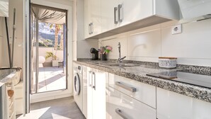 Une cuisine moderne avec des armoires blanches, un comptoir en granit, un lave-linge intégré et une porte-fenêtre coulissante donnant sur un balcon.
