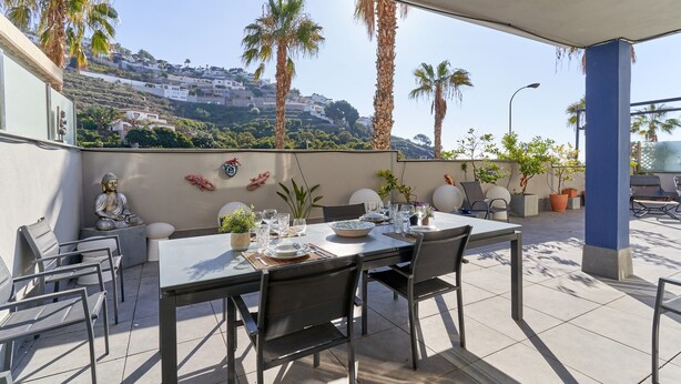 Un espace de restauration en plein air avec une table dressée pour quatre personnes, entourée de chaises, et offrant une vue sur une colline et des palmiers.