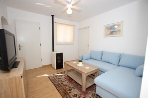 A modern living room with a light blue sofa, a wooden coffee table, a television on a wooden stand, a fireplace, and a ceiling fan. - Holiday Home 'La Casita' with Sea View, Wi-Fi and Air Conditioning (Mutxamel)