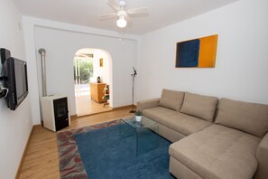 A living room with a sofa, a glass coffee table, a TV, and a ceiling fan.