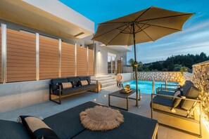 A modern outdoor living area with a pool, seating, and a stone wall.