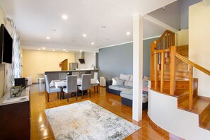 A modern living room with a dining area, a staircase, and a kitchen in the background.