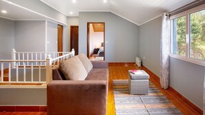 Ein Zimmer mit einer Couch, einem kleinen Tisch, einem fenster mit Vorhängen, einer Treppe und Blick auf ein weiteres Zimmer.