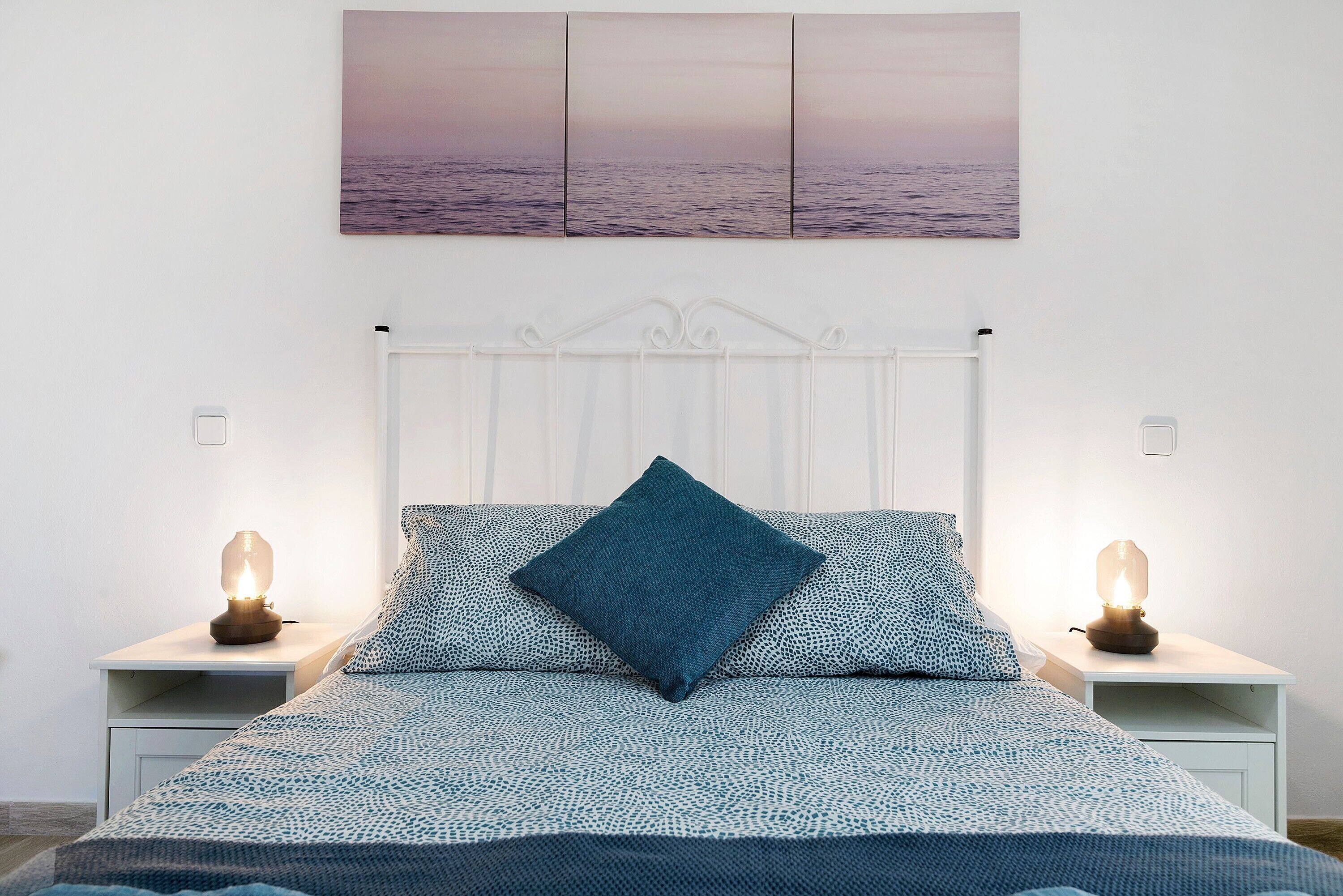 Een bed met een geborduurd sprei, één blauw kussen en twee bedlampjes.