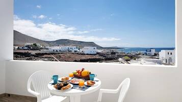 A balcony with a table set for breakfast, overlooking a coastal village with white buildings and a clear sky.