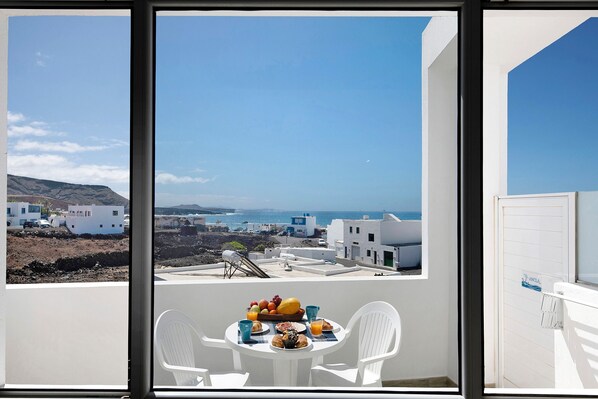 A balcony with a table set for breakfast, overlooking a coastal town with white buildings and a clear blue sky.