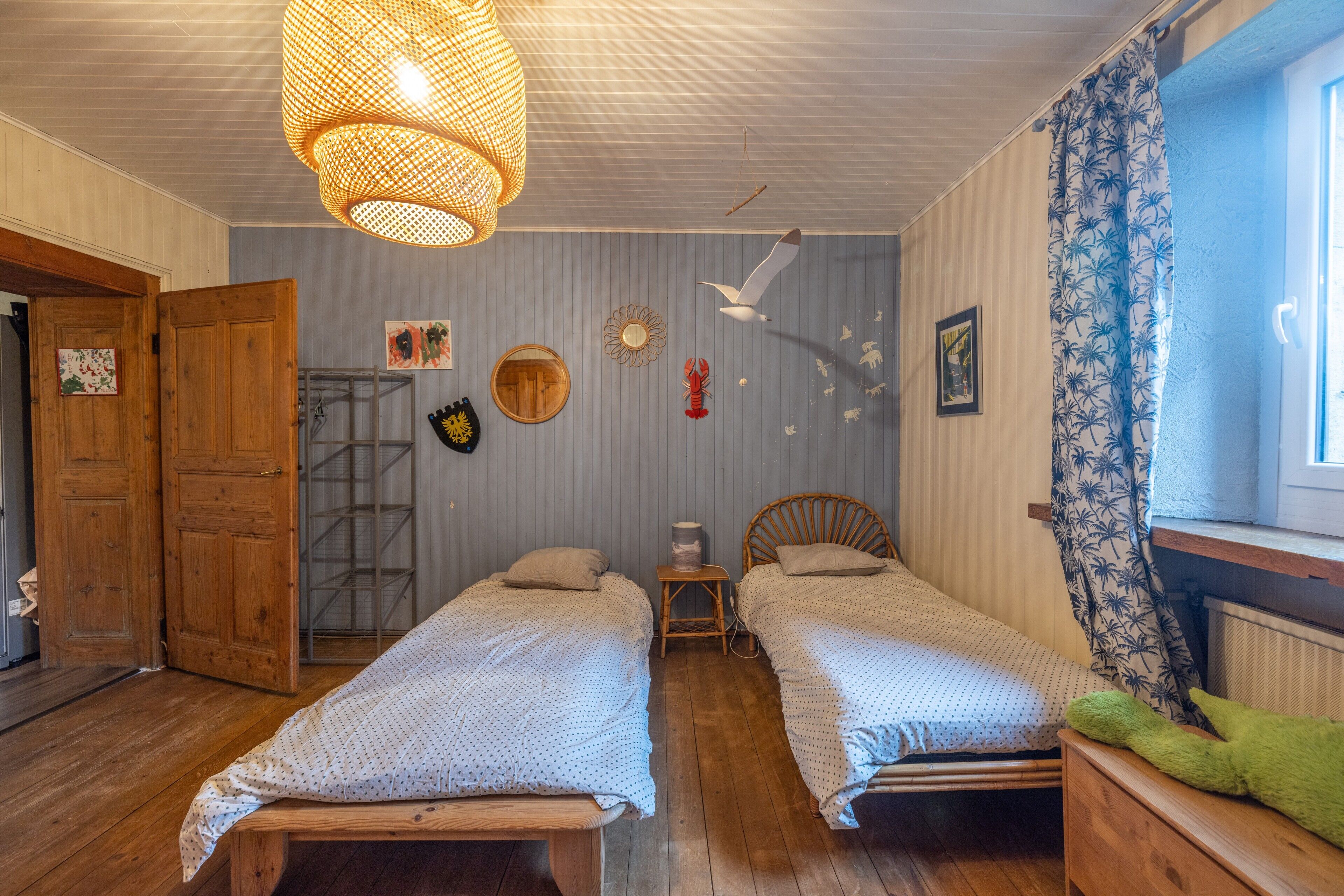 Ein Zimmer mit zwei hölzernen Betten, einer Hängeleuchte, einem Fenster mit Vorhängen und einer Tür.