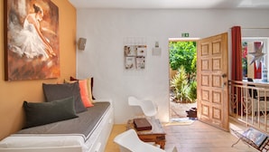 A hotel room with a bed, a white chair, a wooden table, a painting on the wall, and a door leading to an outdoor area. - Holiday Home 'Casa Felix Number 2' with Shared Pool, Shared Terrace and Wi-Fi (Loulé)