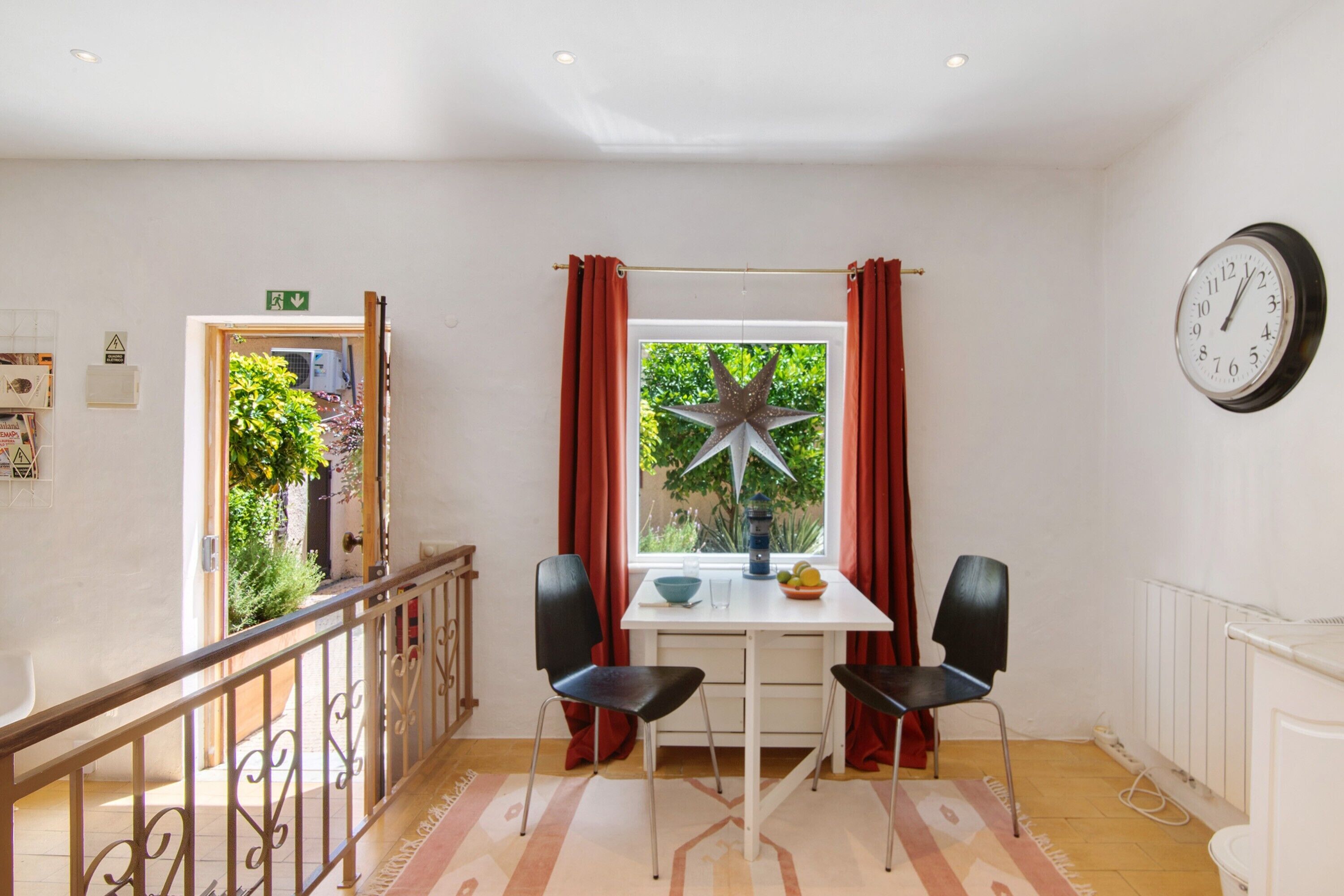 A room with a table, two chairs, a window with curtains, a star decoration, a clock, and a radiator.