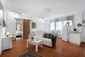 A modern living room with a sofa, coffee table, and a kitchen area with a refrigerator and sink.