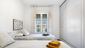 A bedroom with two beds, a window with a view, and a wall-mounted artwork.