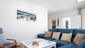 A living room with a blue sofa, a glass coffee table, and a painting of a beach scene.