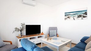 A modern living room with a flat-screen TV, a coffee table, and two blue sofas.