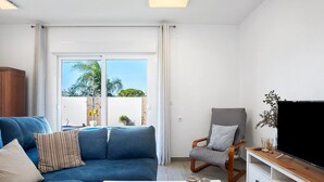 A modern living room with a blue sofa, a wooden chair, a TV on a wooden stand, and a glass coffee table.