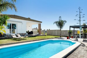 Piscina com espreguiçadeiras, um alpendre coberto e uma casa com telhado em azulejos.