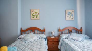 Un dormitorio con dos camas de madera, una mesita de noche con lámpara y decoración floral en la pared.