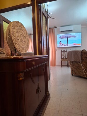 A room with a wooden cabinet, a television displaying a beach scene, a chair, and a bed with a blanket.