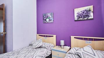 A bedroom with two single beds, a nightstand, a lamp, and two wall-mounted pictures.