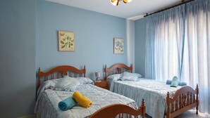 Une chambre à coucher avec deux lits en bois, une table de chevet, une lampe et une fenêtre avec des rideaux.