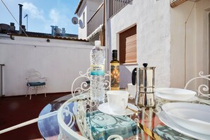 A table set with plates, a cup, a bottle, and a coffee pot on a balcony with a white chair and a metal chair in the background.