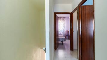 Un estrecho pasillo que conduce a un dormitorio con cama y sillón, puertas de madera y suelo de baldosas.