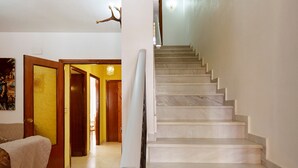 Un escalier avec une rampe, un couloir avec des portes et un mur muni d’un luminaire.