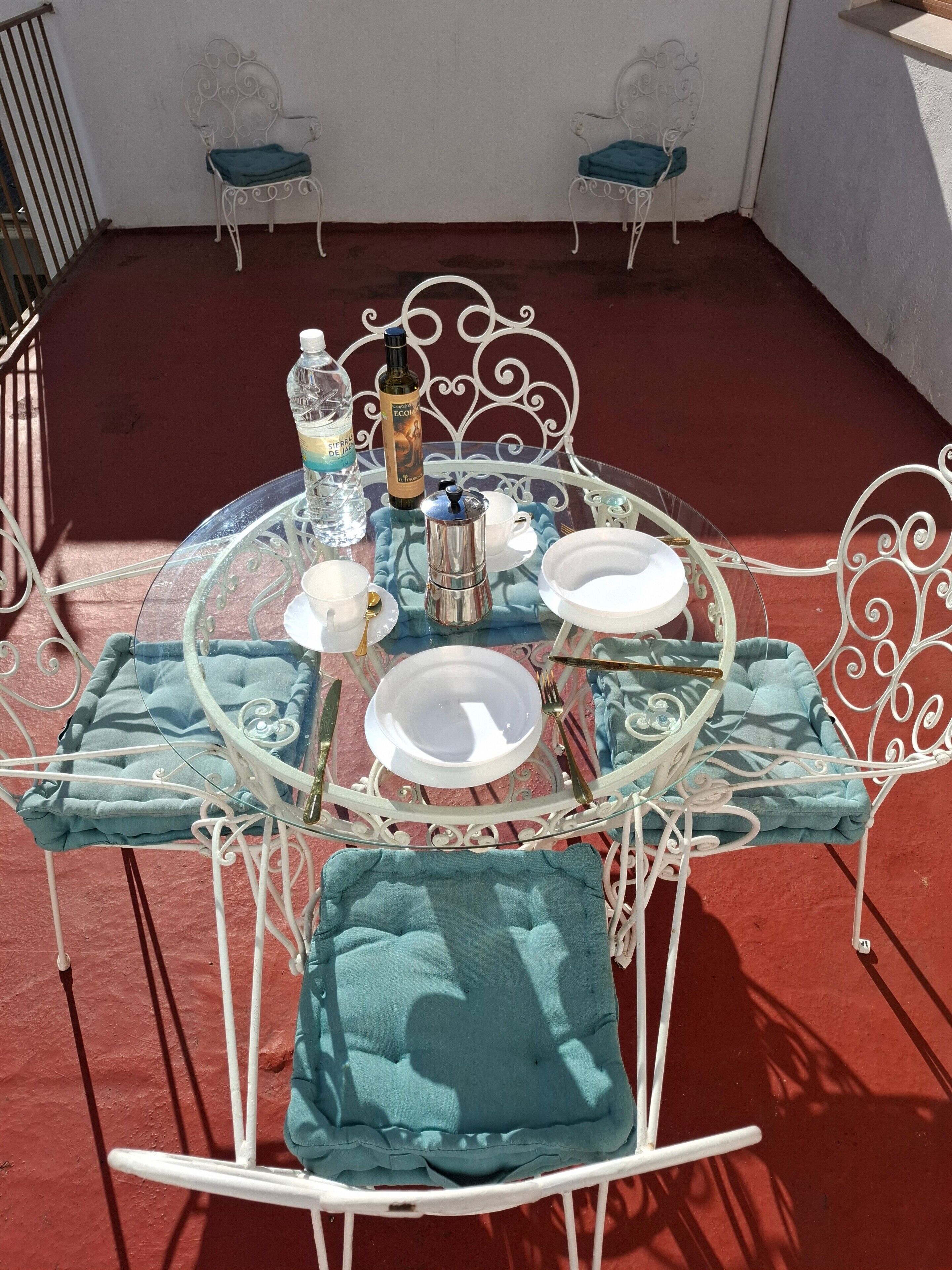 Une table ronde en verre, des chaises en métal, une cafetière et une bouteille d’eau.