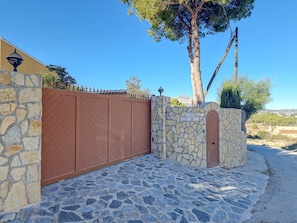 Um muro de pedra com um portão de metal, uma porta de madeira e uma placa com o texto 'CASA FORTUNATA'.