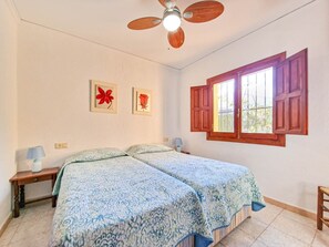 Un dormitorio con dos camas, un ventilador de techo, una ventana con contraventanas de madera y dos lámparas de pared.