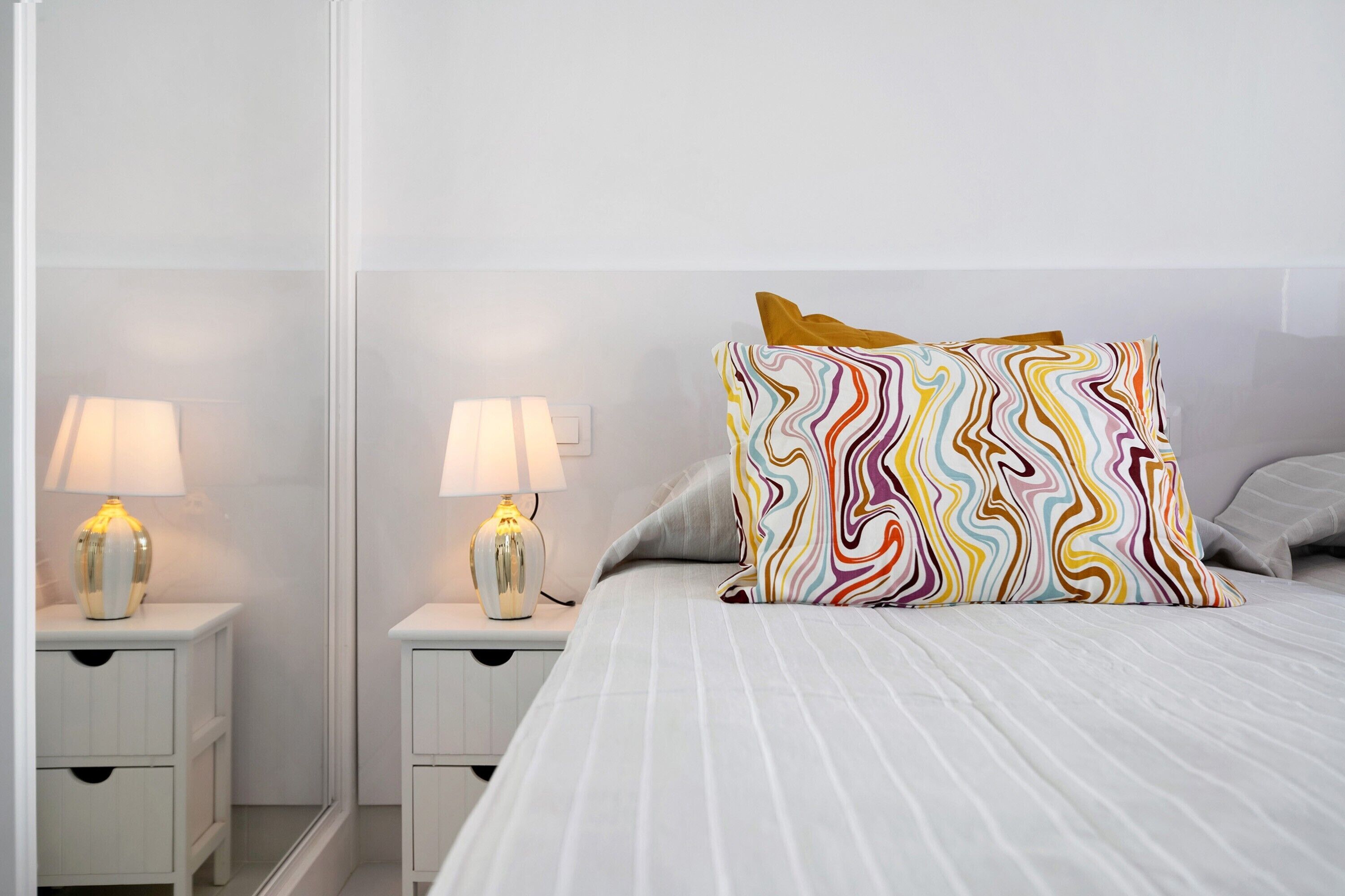 A neatly arranged bedroom with a bed, two bedside tables with lamps, and a mirror.