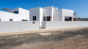 Un edificio moderno con techo plano, entrada protegida por una reja y cielo despejado.