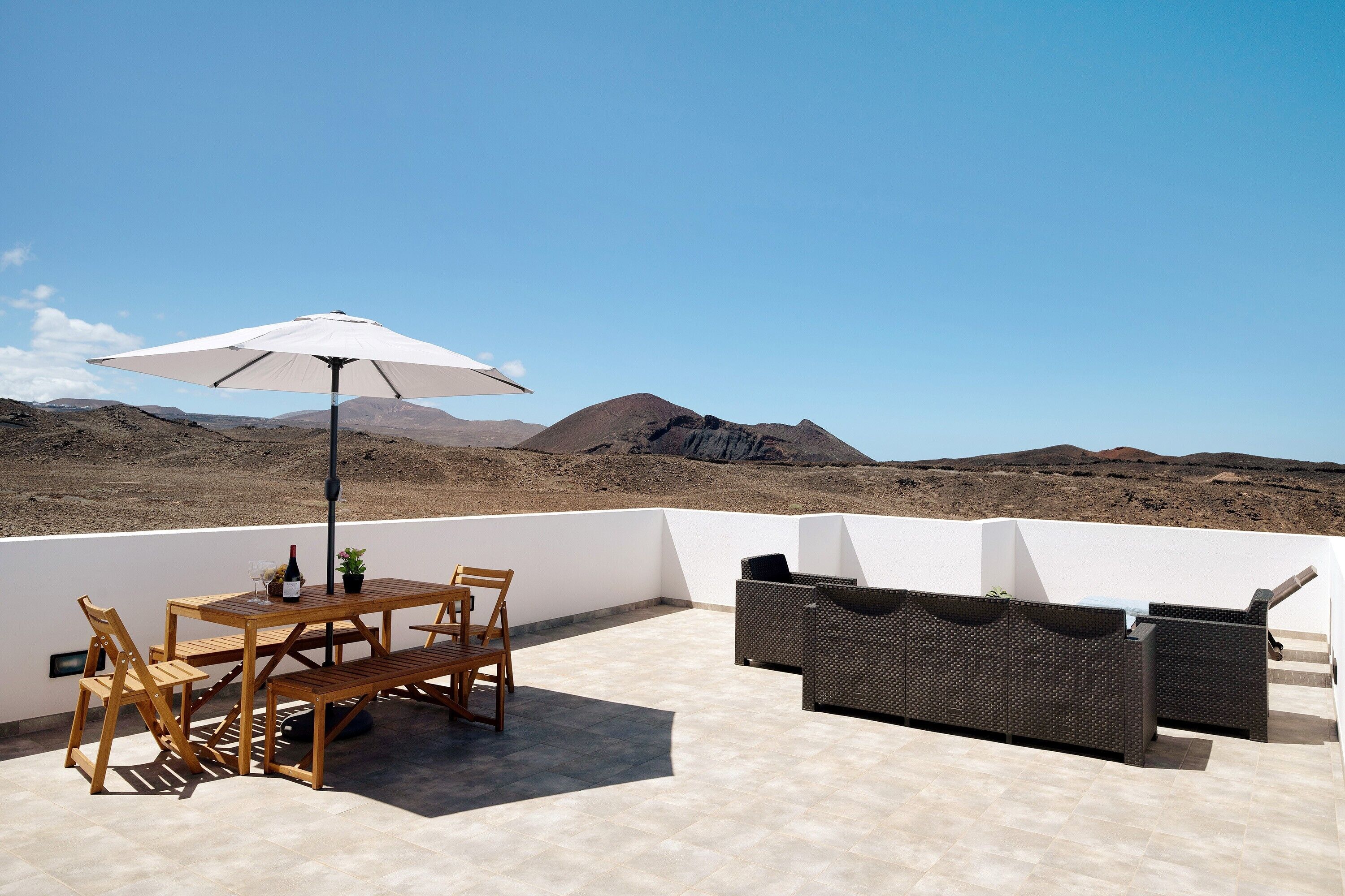 A terrace with a table, chairs, an umbrella, and a sofa.